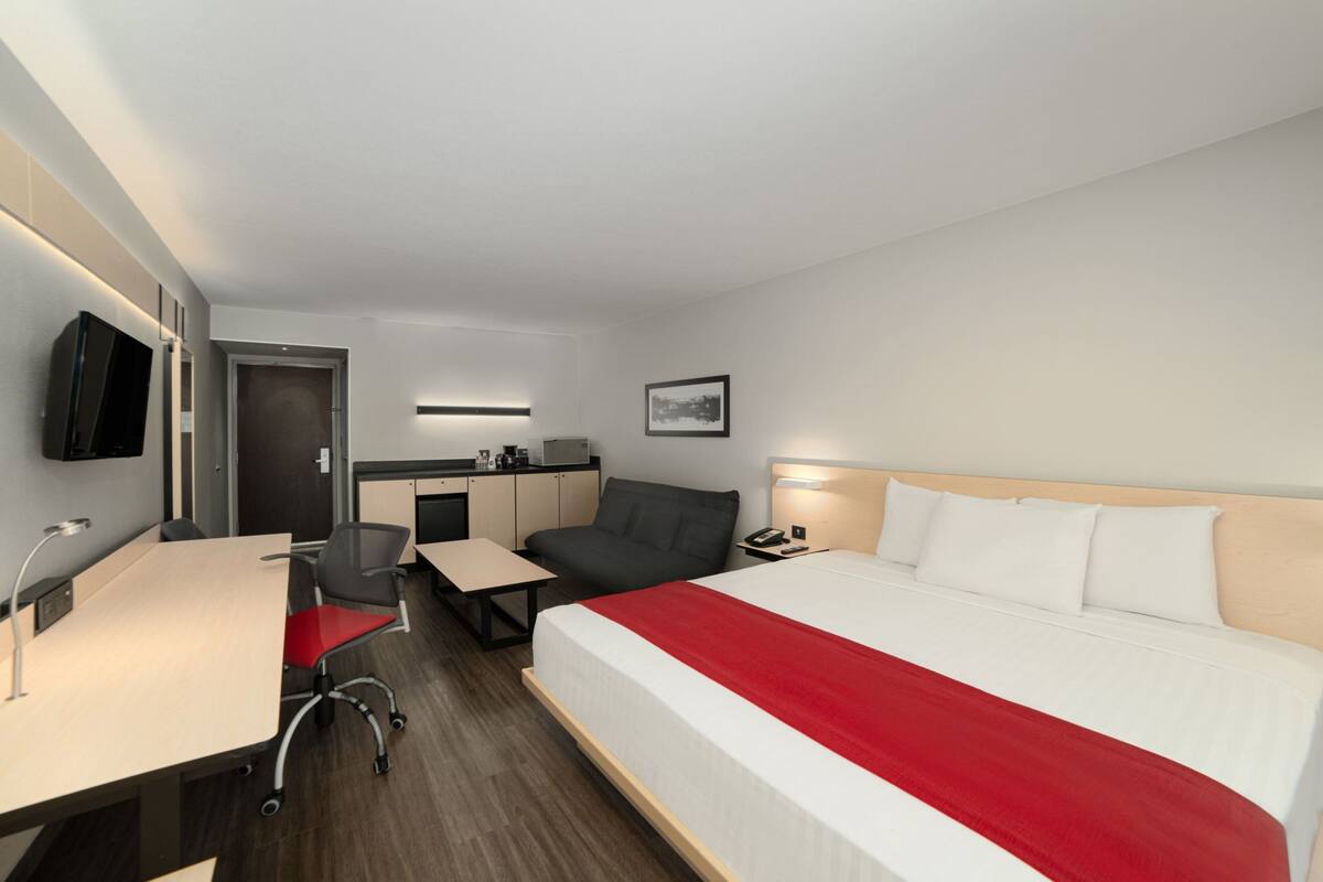 Habitación de hotel con cama, escritorio, silla y una pequeña kitchenette.