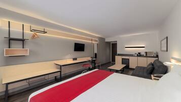 Una habitación de hotel moderna con cama, escritorio, silla, sofá, televisor y kitchenette.