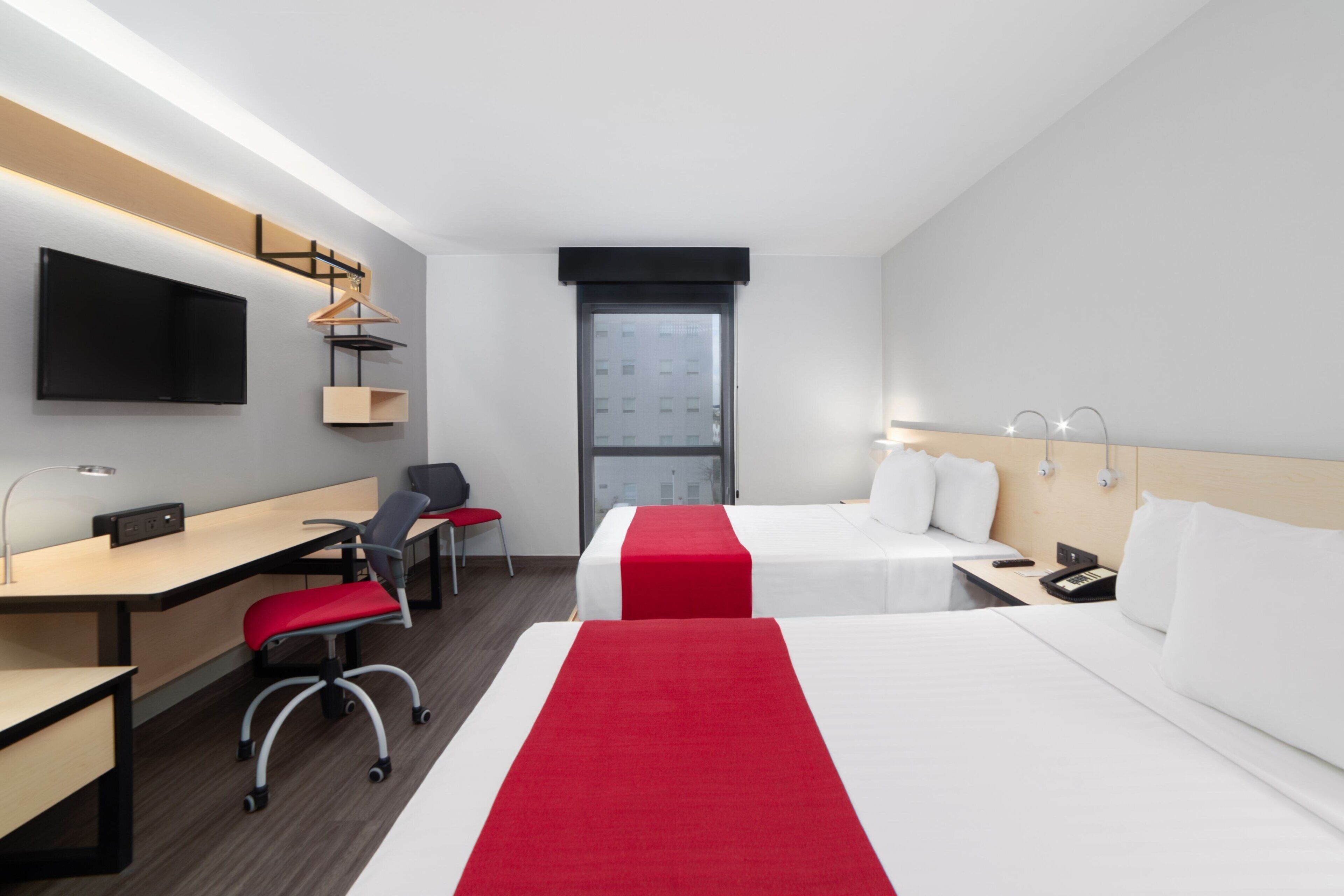 Habitación de hotel con dos camas, un escritorio, una silla, un televisor y una ventana.