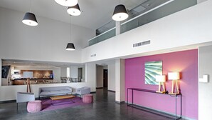 Un vestíbulo espacioso con techo alto, mobiliario moderno y una pared de acento en color rosa vibrante.