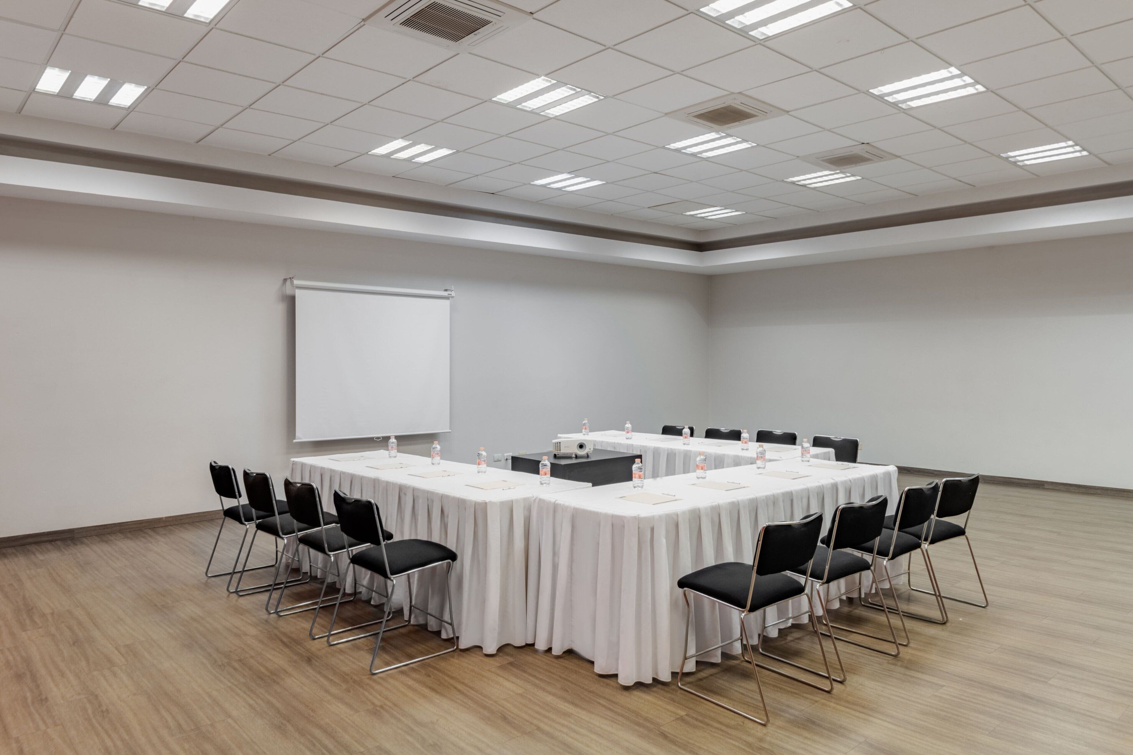 Un salón de conferencias con una larga mesa, sillas negras, una pizarra y un proyector.