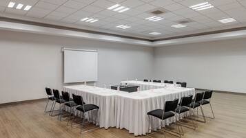Un salón de conferencias con una larga mesa, sillas negras, una pizarra y un proyector.