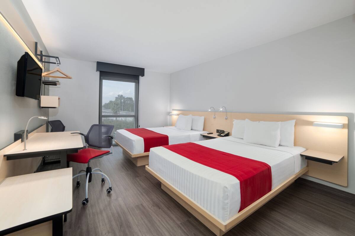 Habitación de hotel con dos camas, un escritorio, una silla, un televisor y una ventana.