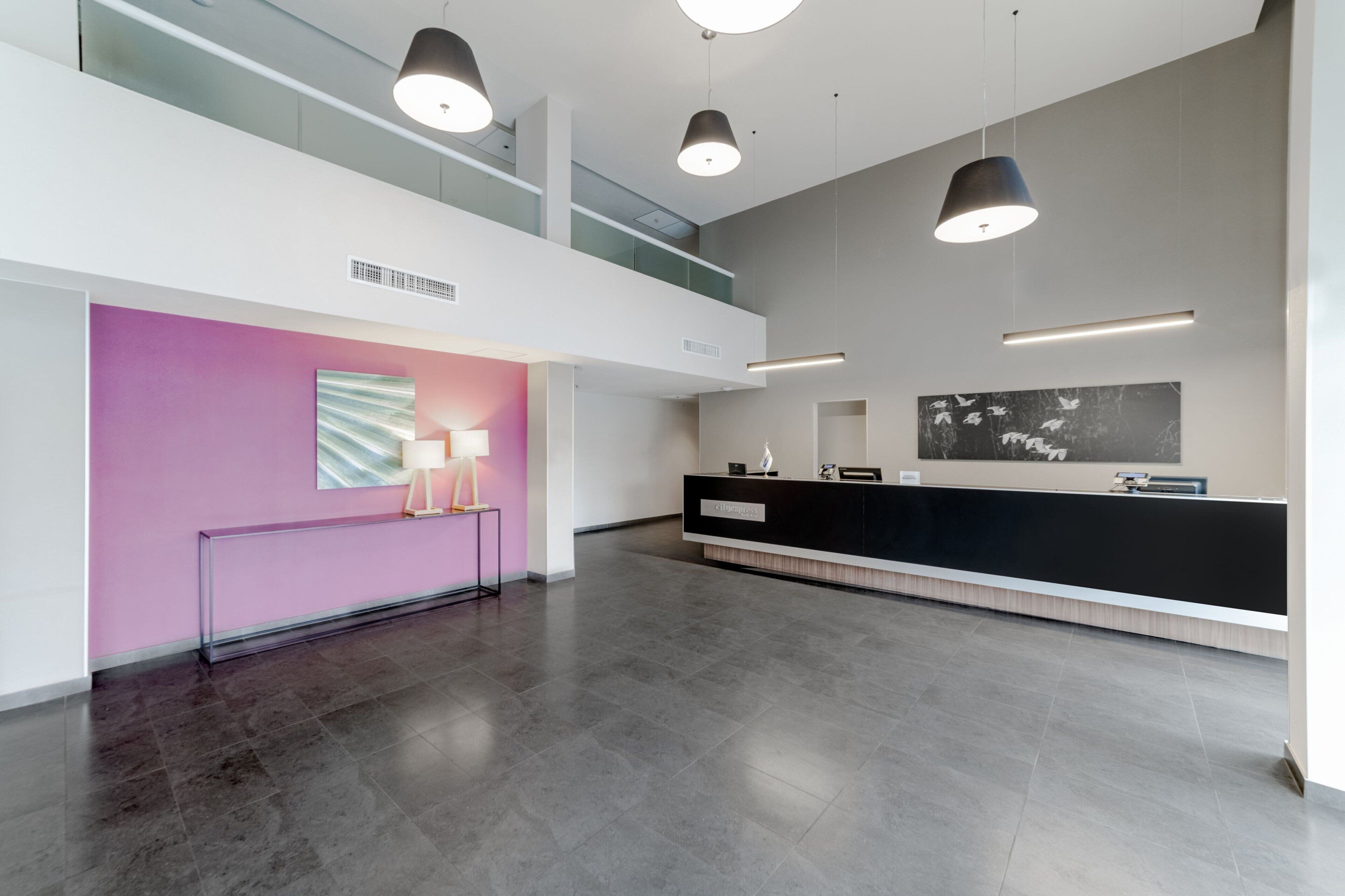 A modern reception area with a black reception desk, a pink accent wall, and a large black and white artwork.