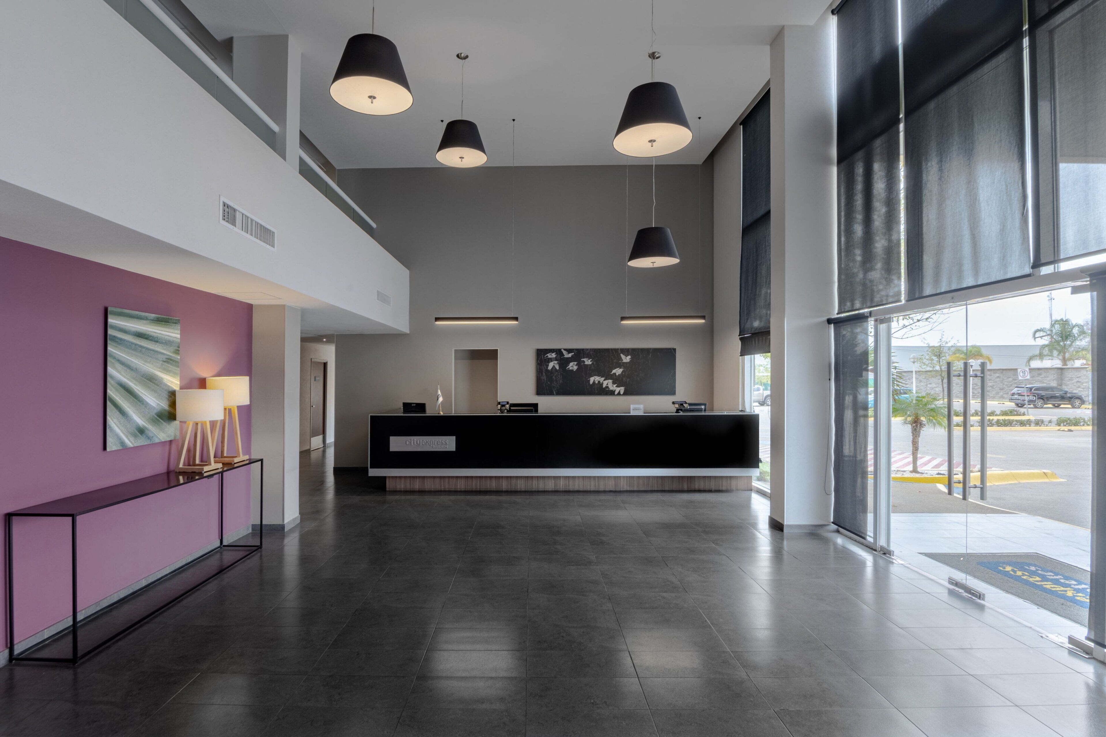 A modern reception area with a black counter, pendant lighting, and a large window offering a view of the street.
