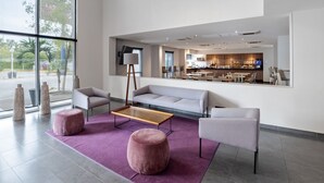 Un moderno vestíbulo de hotel con un sofá, sillones, una mesita de centro y un amplio ventanal con vistas a la calle.