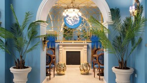 A grand hallway with a white fireplace, two potted plants, and a chandelier. - Grande Bretagne (Nafplio)