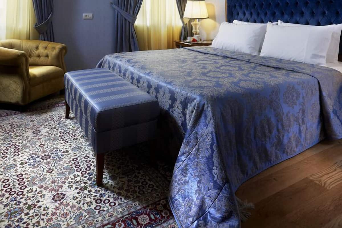 Ein Schlafzimmer mit einem großen Bett, einem durchgestellten Kopfteil, einer Chandelüster und einem gemusterten Teppich.