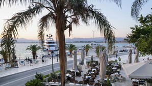 A waterfront restaurant with outdoor seating, palm trees, and boats in the background. - Grande Bretagne (Nafplio)