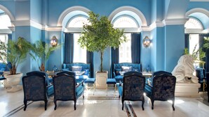 A room with blue walls, a large tree, and a statue. - Grande Bretagne (Nafplio)