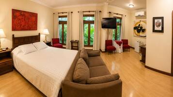 A hotel room with a large bed, a sofa, a TV, and a dining area with chairs.