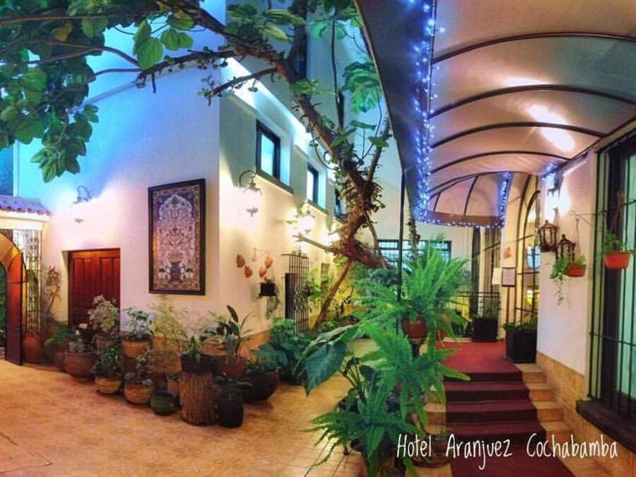 Interior de hotel com um pátio, plantas em vasos e escadas que levam ao andar superior.