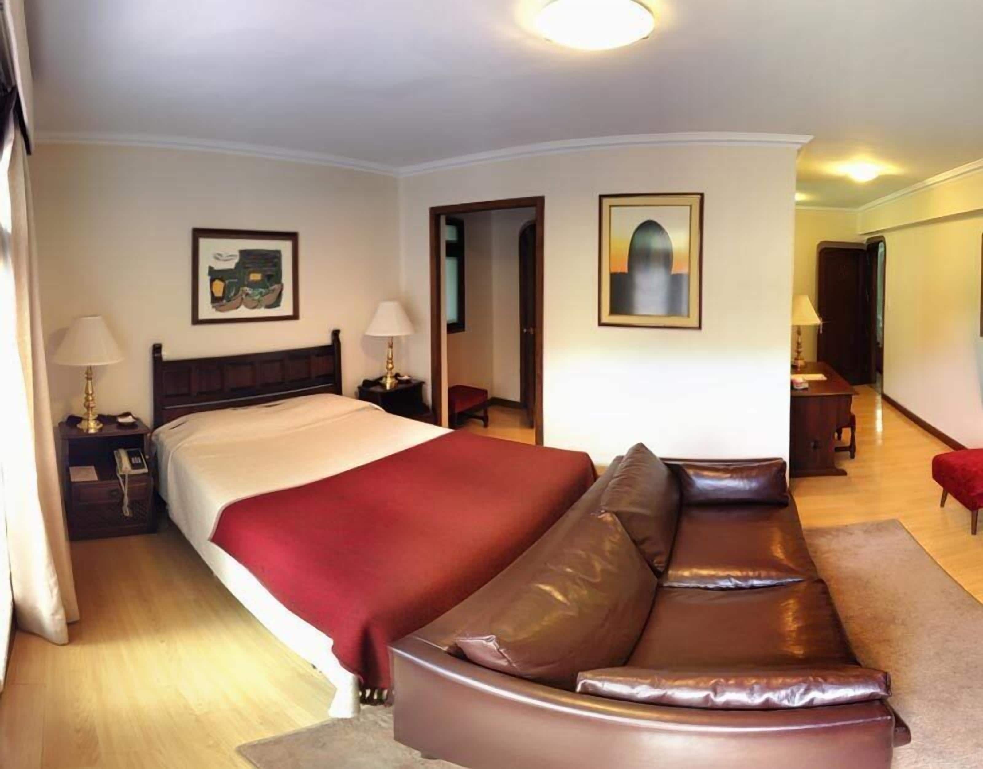A hotel room with a large bed, a leather sofa, a desk, and a chair.
