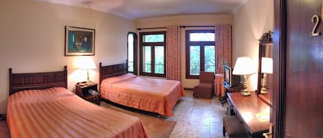Una habitación de hotel con dos camas, un escritorio con lámpara, una silla y un televisor.