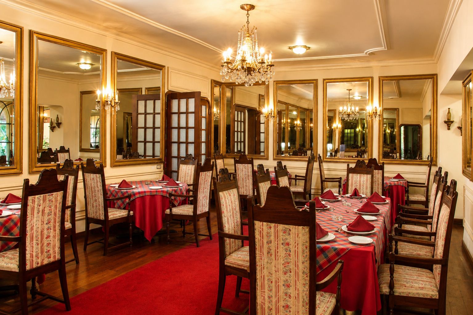 A formal dining room with multiple tables set for service, large mirrors on the walls, and a chandelier.