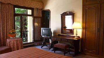 A hotel room with a bed, a desk with a lamp, a television, and a large mirror.