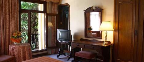 Habitación de hotel con cama, escritorio con lámpara, televisión y un espejo grande.
