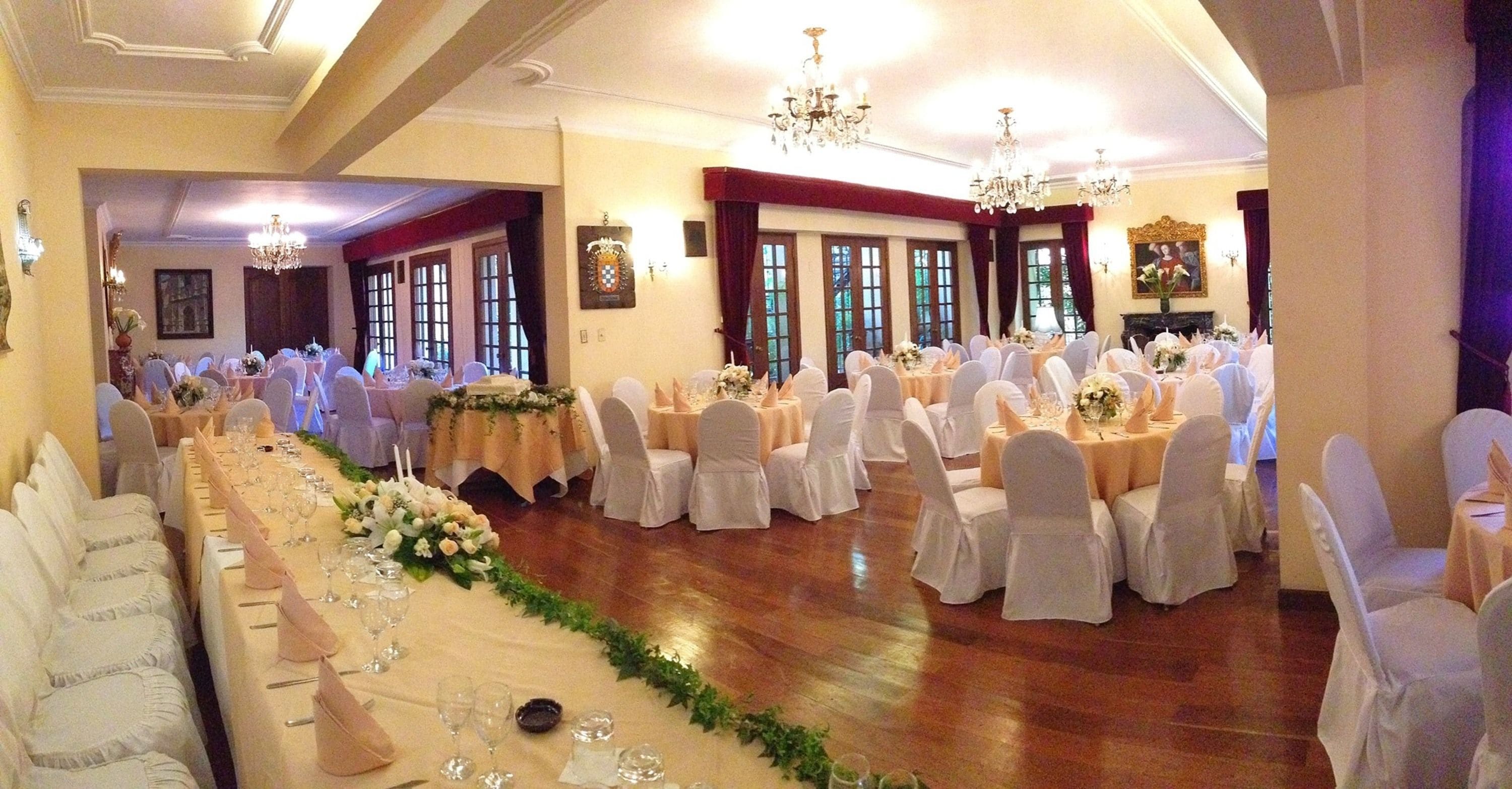 Un salón de banquetes con largas mesas dispuestas para un evento formal, con candelabros y centros de mesa florales.