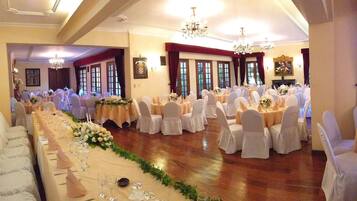 Un salón de banquetes con largas mesas dispuestas para un evento formal, con candelabros y centros de mesa florales.
