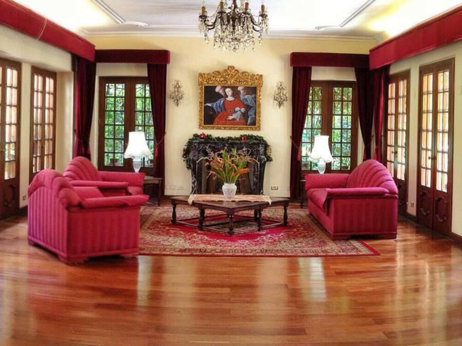 Amplia habitación con suelo de madera, dos sofás rojos, una mesa de centro y una araña.