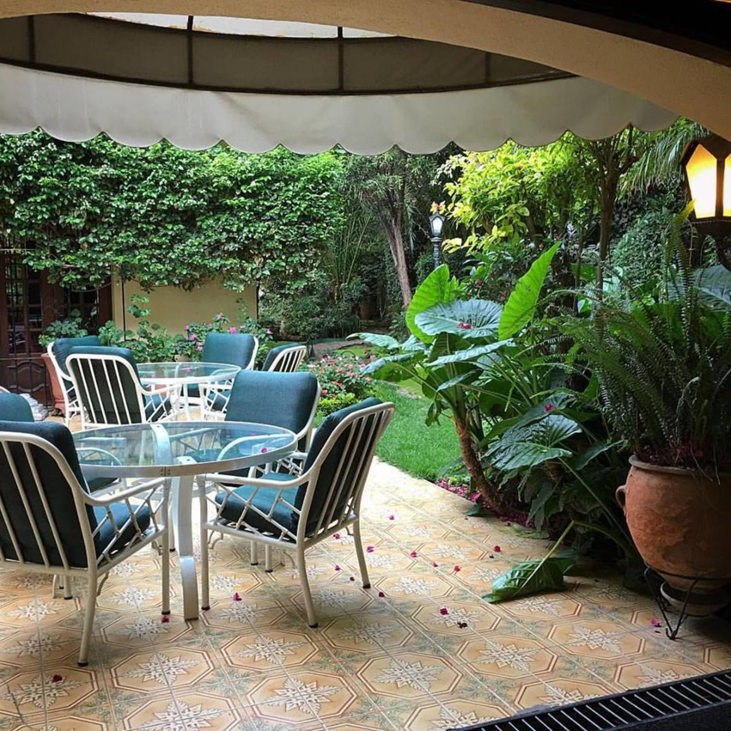 Eine Terrasse im Freien mit Tisch und Stühlen, umgeben von üppigem Grün und einem Fliesenboden.