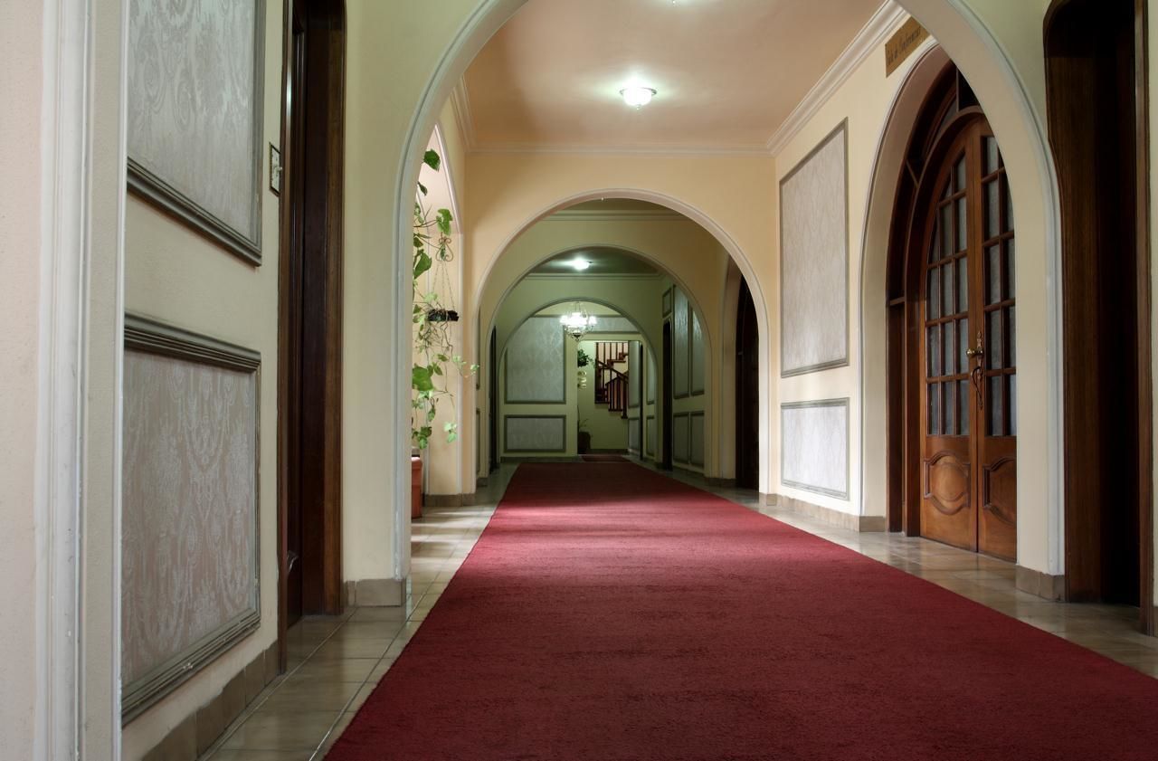 A hallway with a red carpet, arched doorways, and a chandelier.