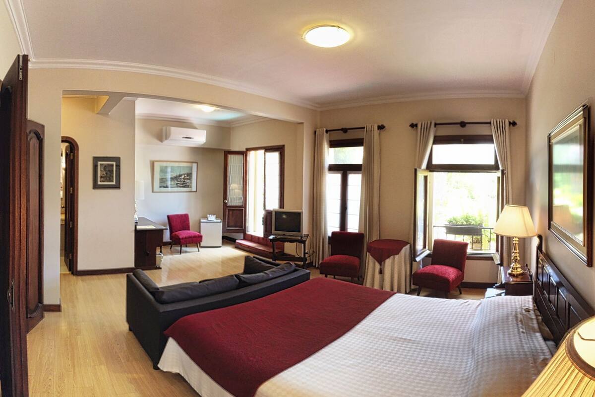 Habitación de hotel con una cama grande, un escritorio con silla, un televisor y una ventana con cortinas.
