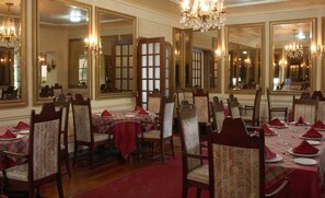 A formal dining room with multiple tables set for service, large mirrors, and chandeliers.