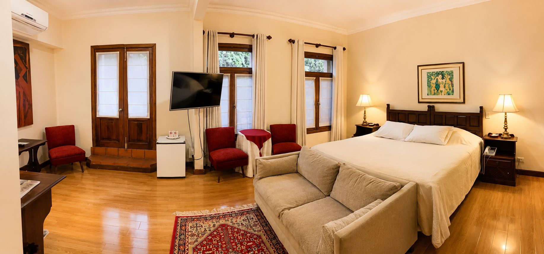 A hotel room with a bed, a TV, a desk, and a red armchair.