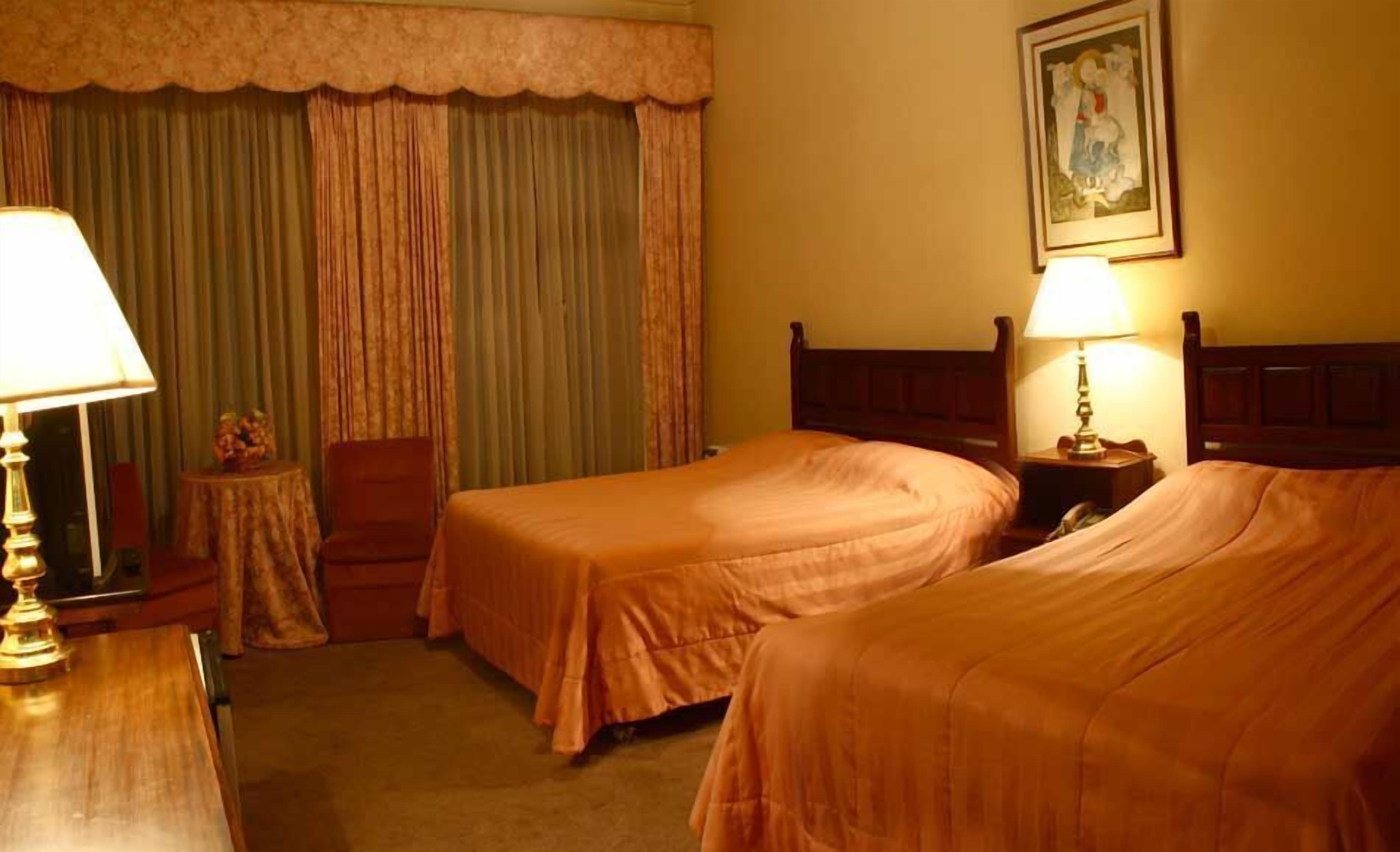 Een hotelkamer met twee bedden, een tafeltje, een stoel en een lamp.