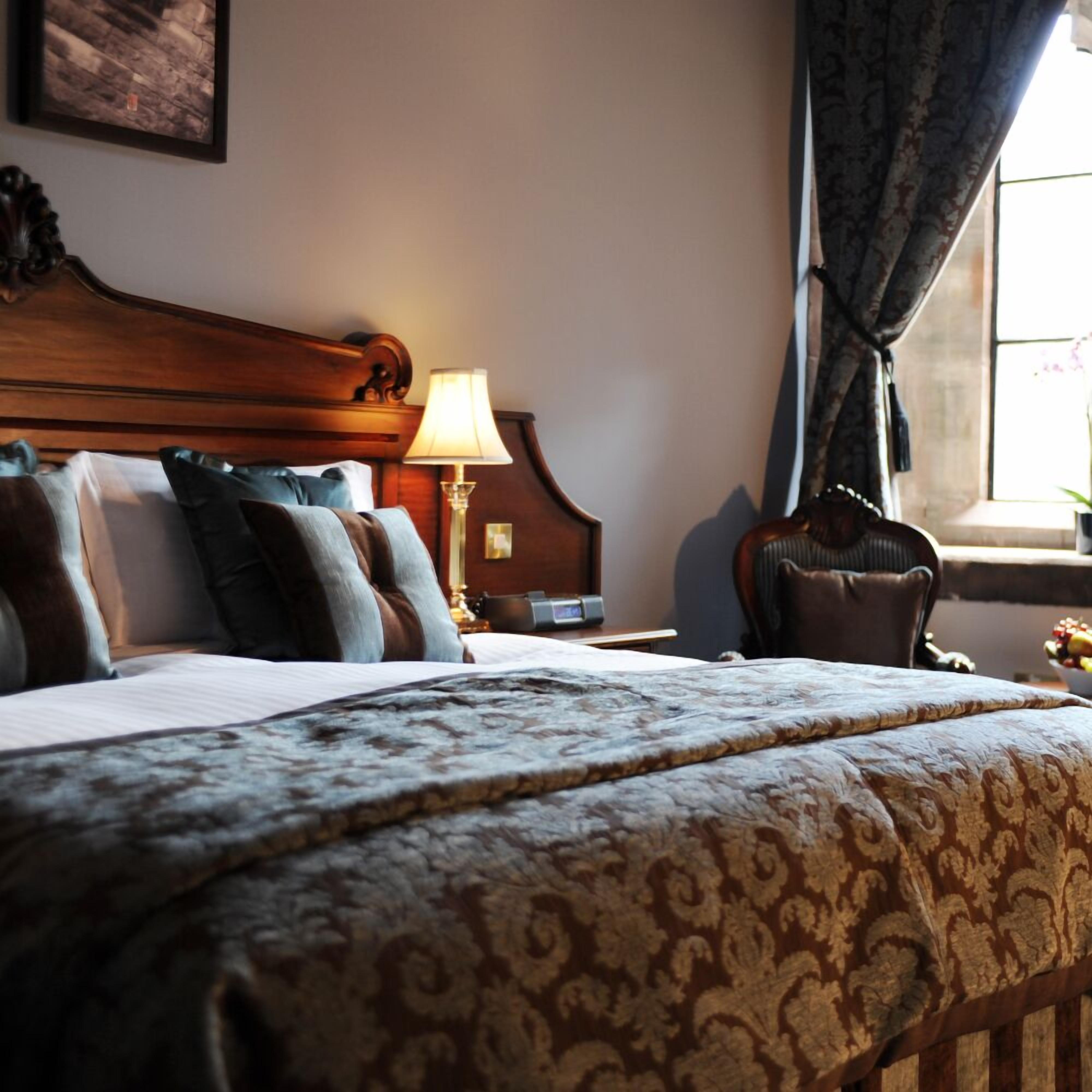 Une chambre d’hôtel avec un grand lit, une tête de lit en bois, une table de chevet avec une lampe et une fenêtre avec des rideaux.