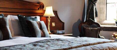 Une chambre d’hôtel avec un grand lit, une tête de lit en bois, une table de chevet avec une lampe et une fenêtre avec des rideaux.