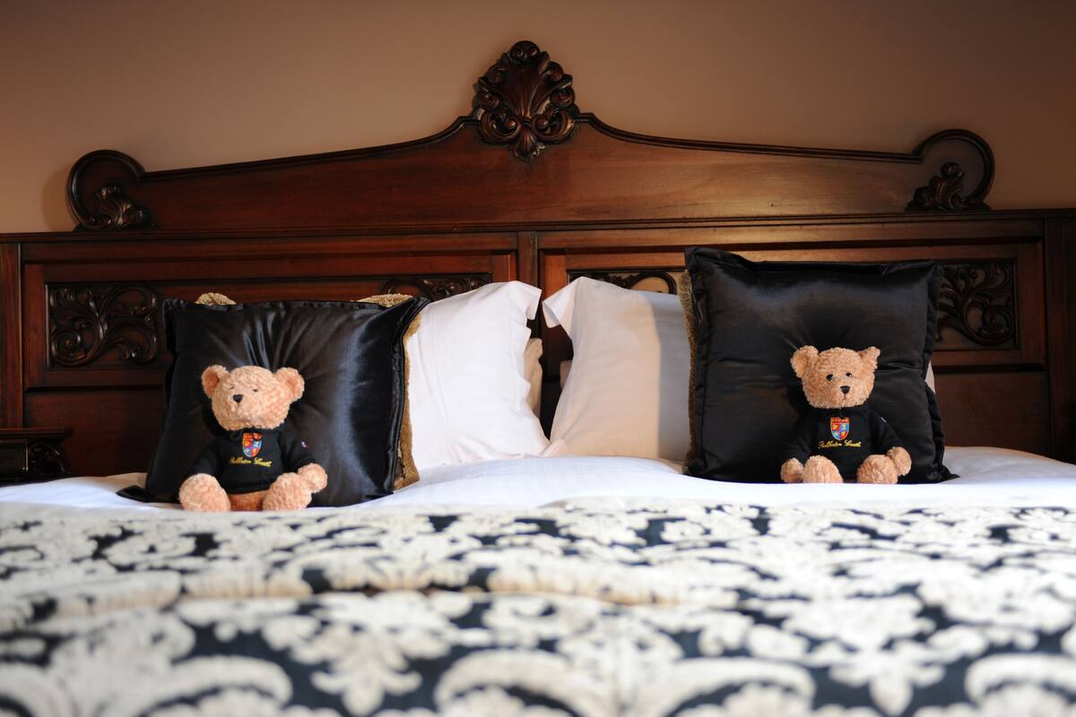 Un lit avec une tête de lit sombre, deux oreillers et deux ours en peluche.