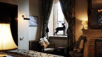 A hotel room with a large bed, a fireplace, a window with a deer sculpture, and a chandelier.