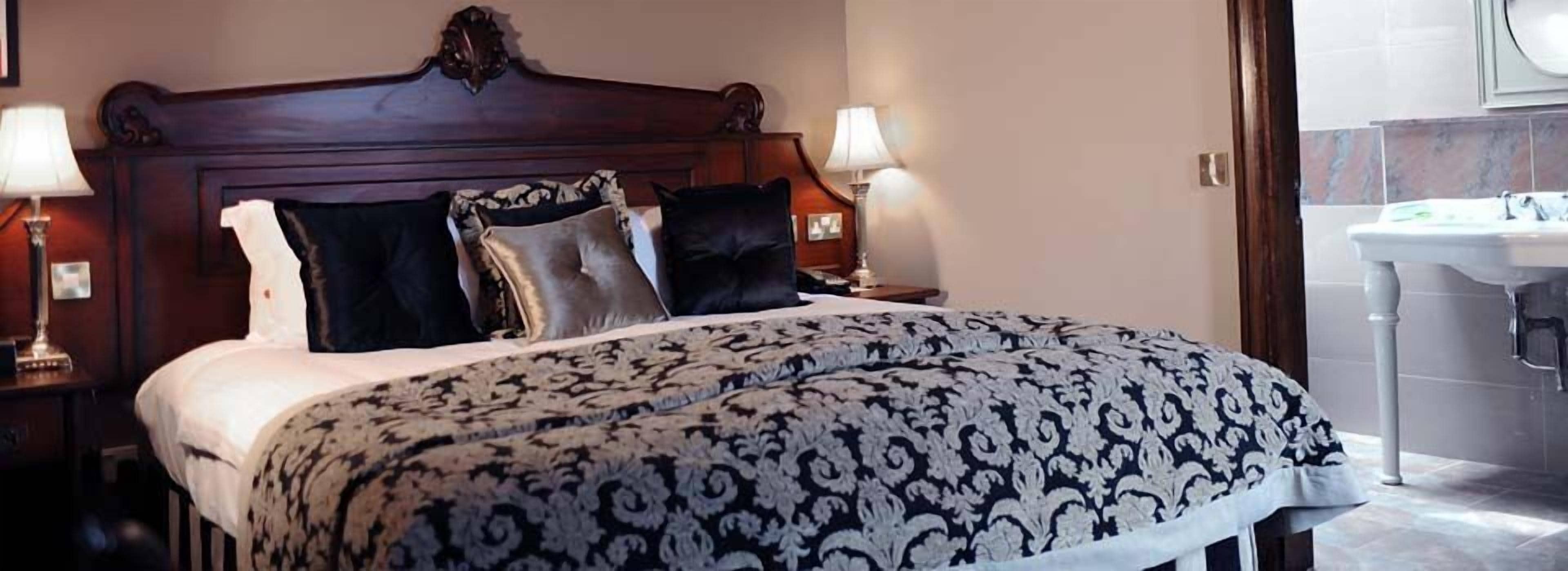 Un letto rifatto con una coperta a motivi, due abat-jour e una testiera in legno.