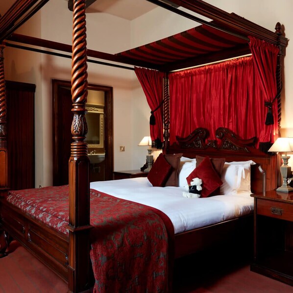 A four-poster bed with a red canopy, wooden headboard, and a red bedspread.