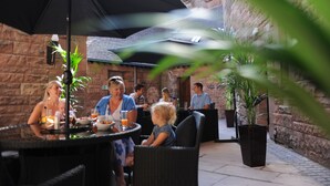 Une terrasse extérieure avec des murs en pierre, des tables rondes et des parasols.