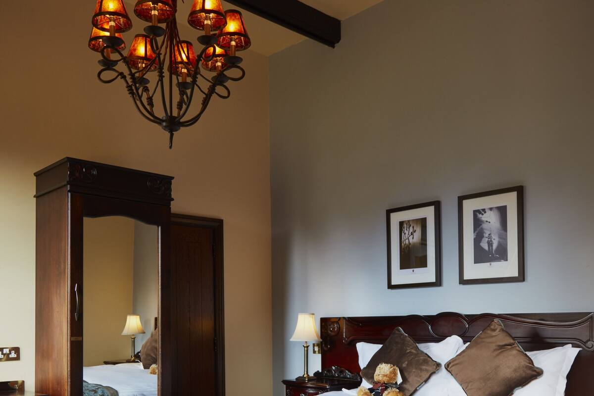 Une chambre à coucher avec un grand lit, une tête de lit en bois, un lustre et deux tableaux encadrés accrochés au mur.