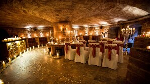 Une salle de banquet aux murs de pierre, ornée de lustres et dont les tables sont dressées pour un événement officiel.