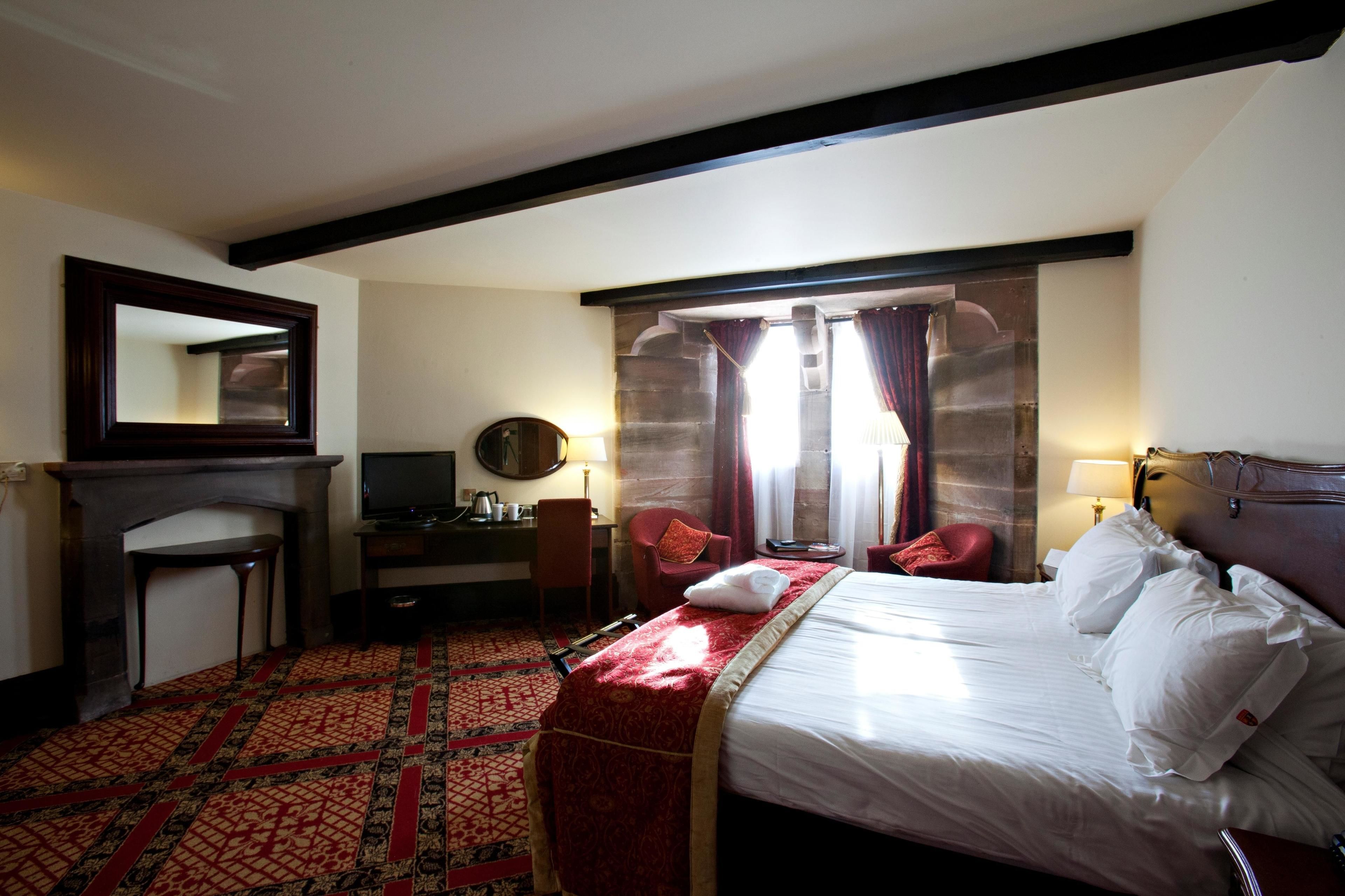 A hotel room with a bed, a desk, a chair, a fireplace, and a large mirror.