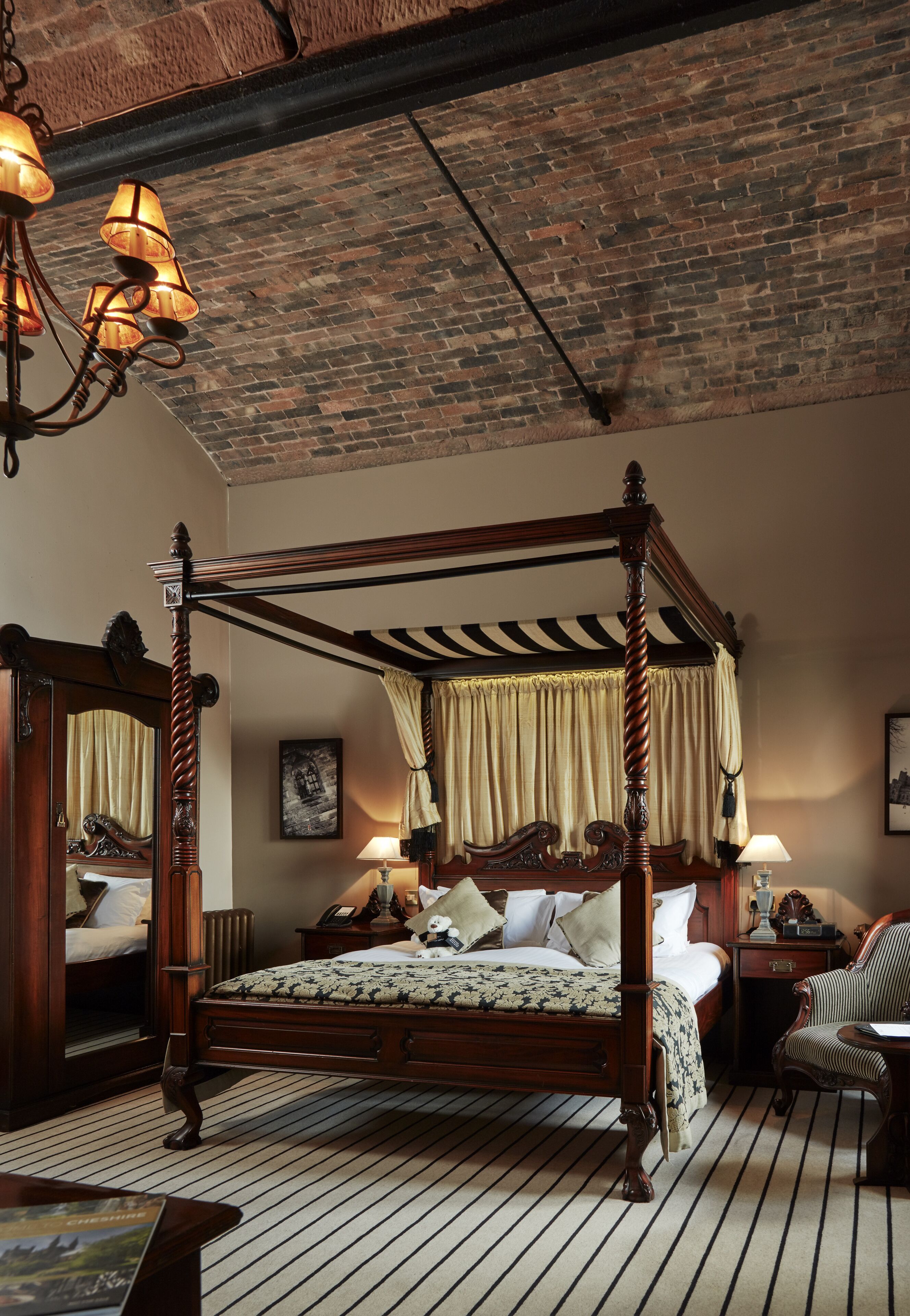 Een hemelbed met houten frame, een spiegel en een nachtkastje met een lamp.
