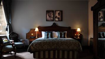 A hotel room with a large bed, two bedside lamps, a wooden headboard, a chair, and two framed pictures on the wall.