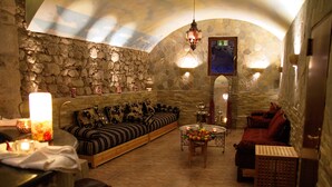 A stone-walled lounge with a sofa, a red couch, and a coffee table with fruit. - Atlas Grand Hotel (Garmisch-Partenkirchen)