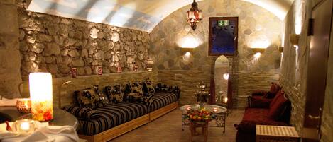 Un salón con paredes de piedra, un sofá, un sofá rojo y una mesa de centro con fruta.