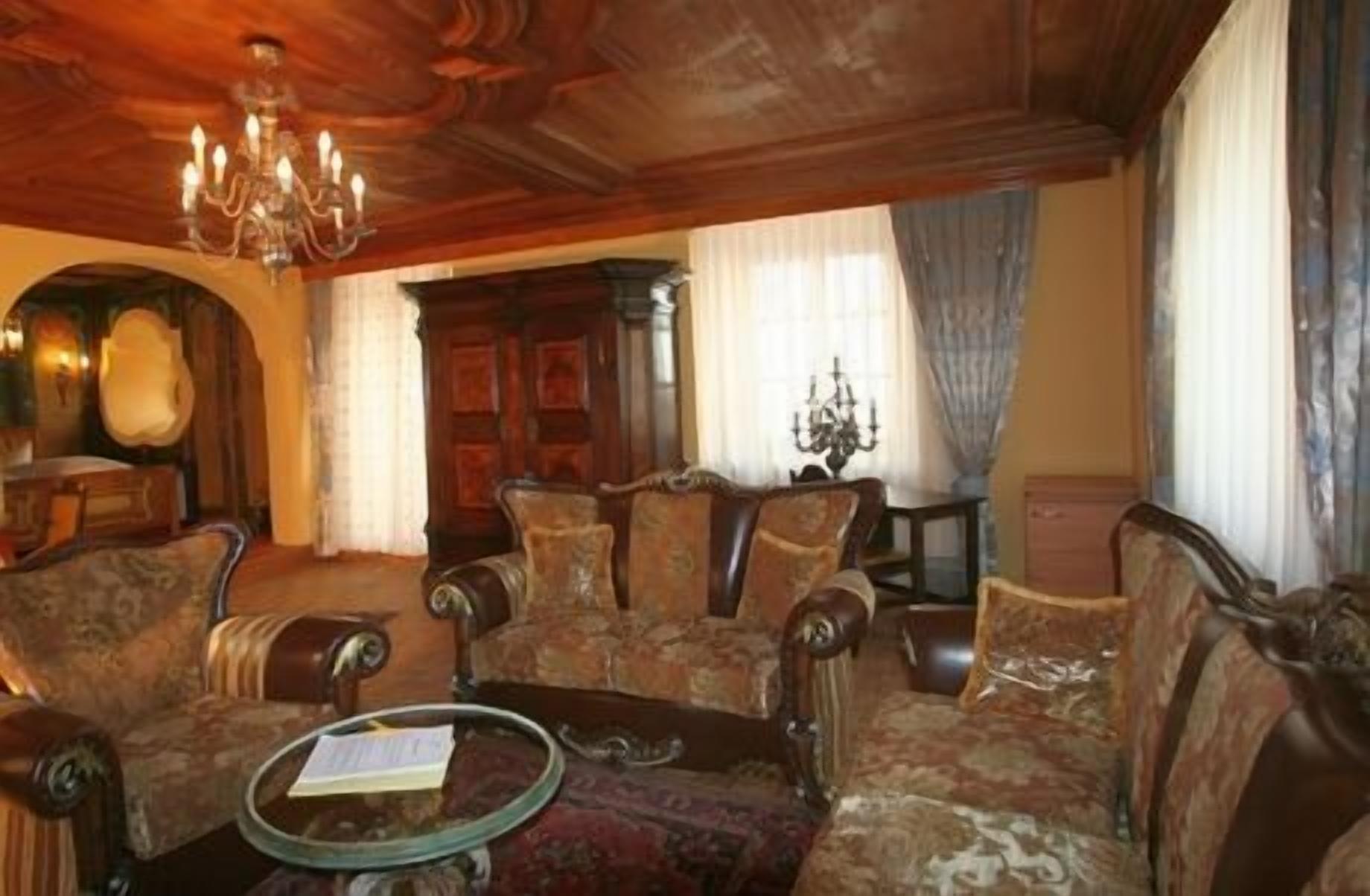 Una habitación tradicional con paneles de madera, un candelabro y muebles clásicos, incluyendo sillones y un sofá.