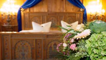 A room with a wooden headboard, a bed with white pillows, and a floral arrangement on the side.