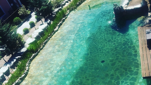 A clear pool with a stone border, surrounded by greenery and a wooden deck. - Atlas Grand Hotel (Garmisch-Partenkirchen)