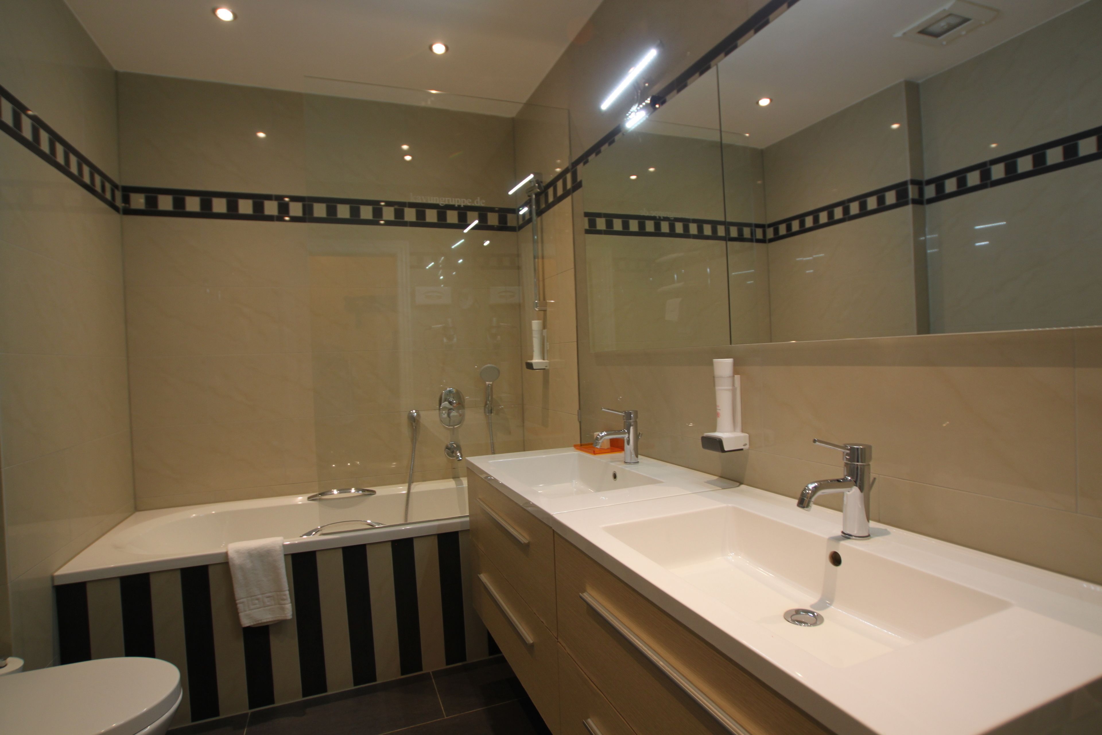 A modern bathroom with a dual sink vanity, a bathtub, and a toilet.