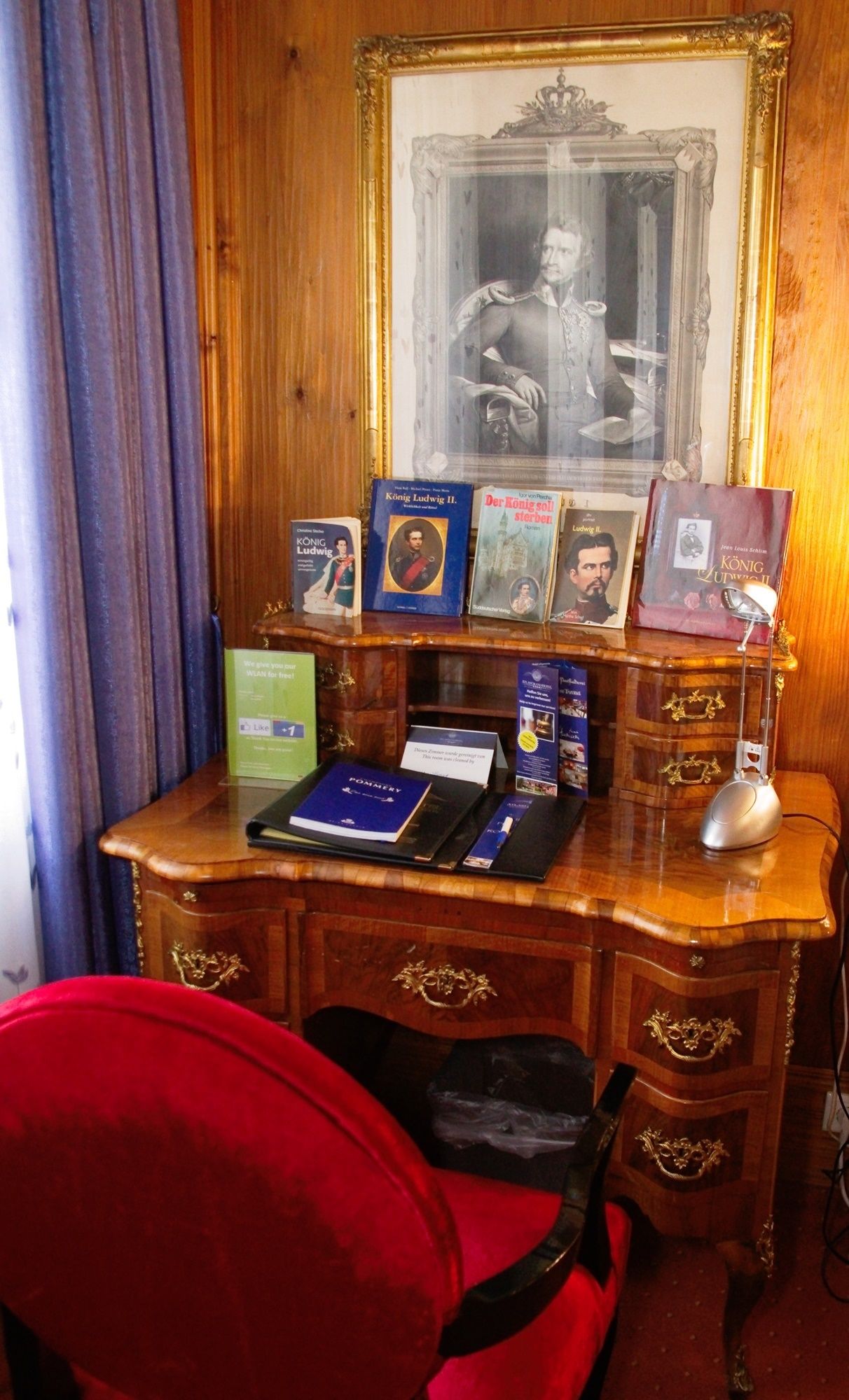 A wooden desk with a framed portrait, several books, a laptop, and a desk lamp.