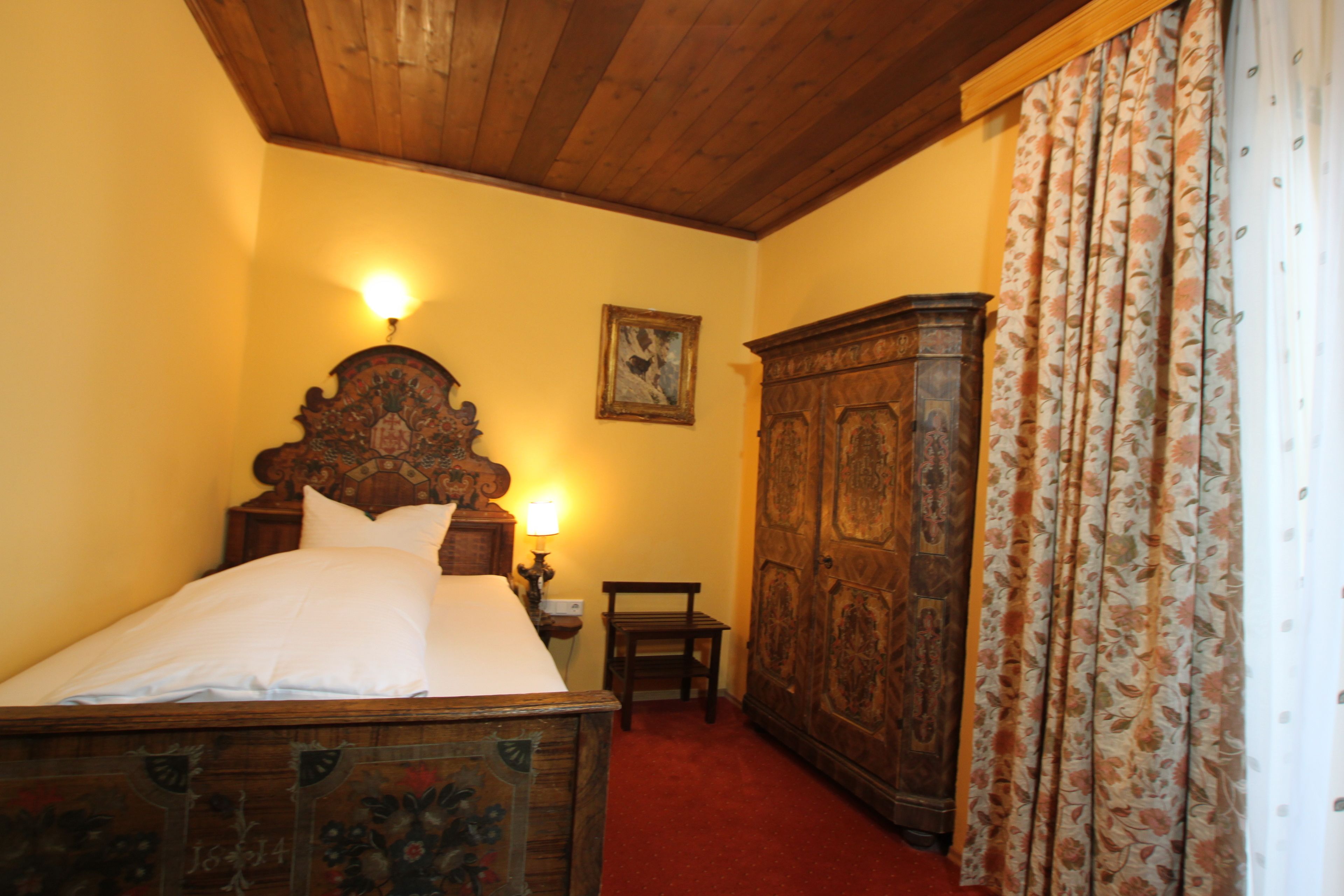 Een slaapkamer met een houten bed, een nachtkastje, een houten kledingkast en een schilderij aan de muur.